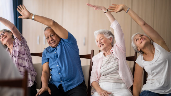Older people sitting on chairs doing arm exercises