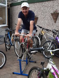 Man on a static bike in garden surrounded by bikes