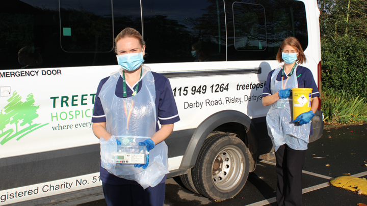 Two nurses standing in front of minibus in PPE