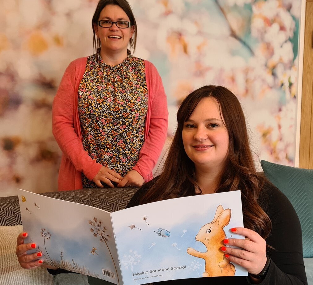 Two women smiling holding bereavement book