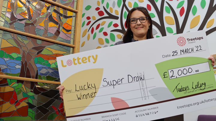 Woman smiling holding Treetops Lottery Super Draw winning cheque