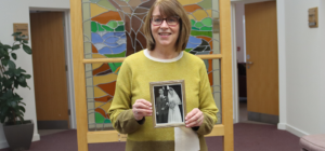 Catherine Mears smiling at camera holding photo of parents
