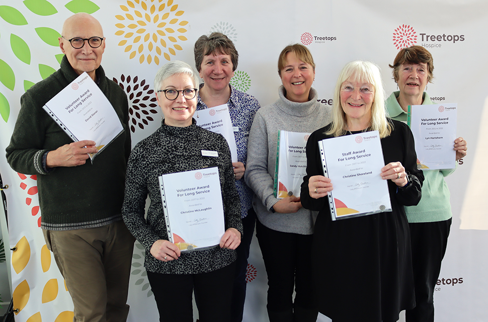 Group of smiling volunteers and staff with long service awards at treetops event
