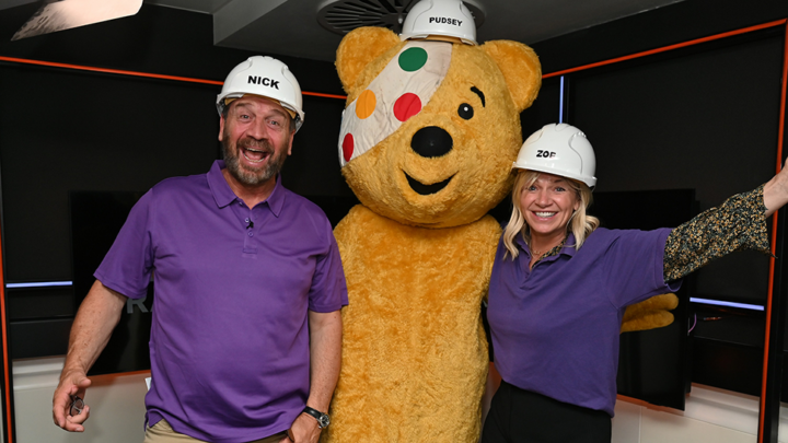Two people smiling with Pudsey Bear from BBC Children in Need