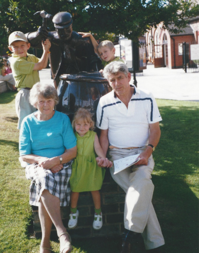 Two grandparents with three children sitting by a statue