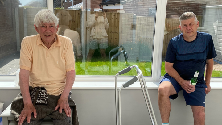 Two men sitting in window of a conservatory smiling