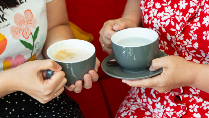 hands of 2 people holding grey mugs of drink