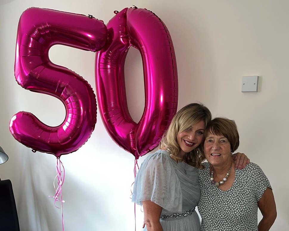 Two women smiling next to pink helium balloons showing '50'
