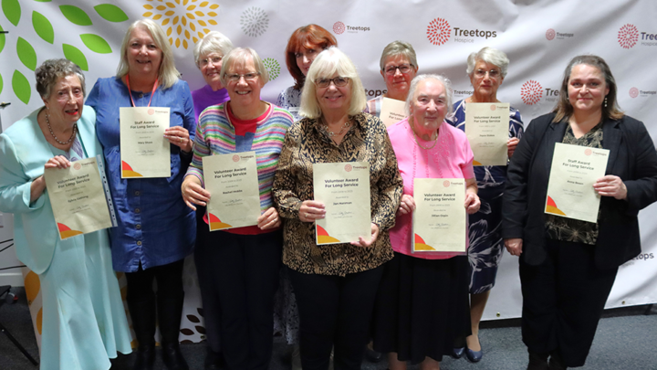 Group of women holding certificates and smiling in front of a Treetops Hospice banner