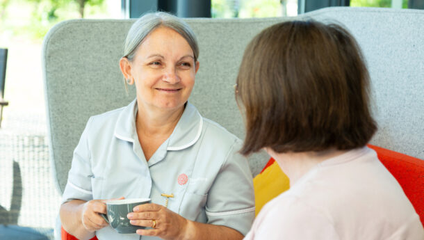 smiling nurse in a grey nursing uniform holding a cup