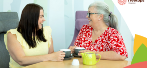 2 women smiling at each other whilst sitting and holding cups