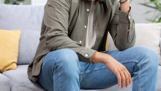 Young asian man sitting on sofa with head in hands looking sad and upset
