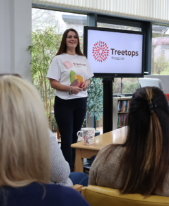 Younf white woman with long dark hair in a treetops Hospice t-shirt giving a talk about the hospice to a local group