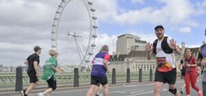 Man in Treetops t-shirt running past Lond Eye on London landmarks half-marathon, giving thumbs up to the camera