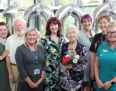 A group of eight people with silver balloons shaped as numbers, probably celebrating an event.