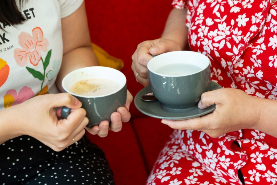 Two people holding coffee cups, one in a red floral dress, the other in a white tee with polka dot pants.
