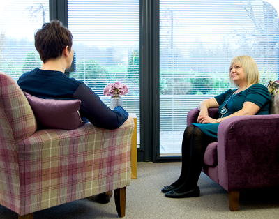 Two people sitting in a room with one looking out a window.