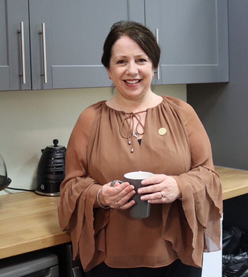 Person in a brown blouse holding a mug in a kitchen.