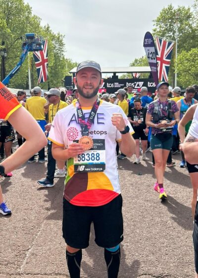 a man wearing a cap who has just run the London marathon holding a medal