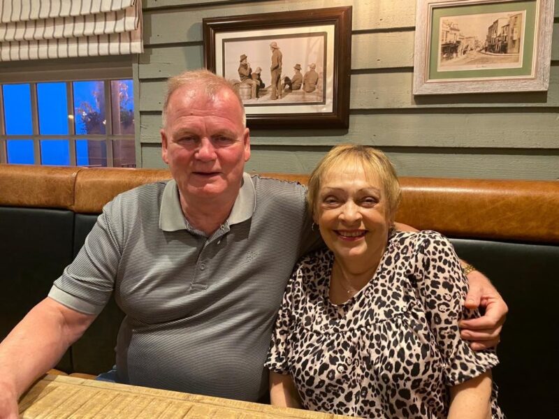 A couple sits together at a cozy restaurant, enjoying their time amidst rustic decor featuring framed artwork and warm lighting.