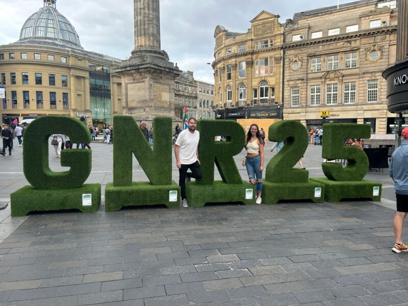 A man and woman stood in front of a big green sign reading 'GNR 25'.