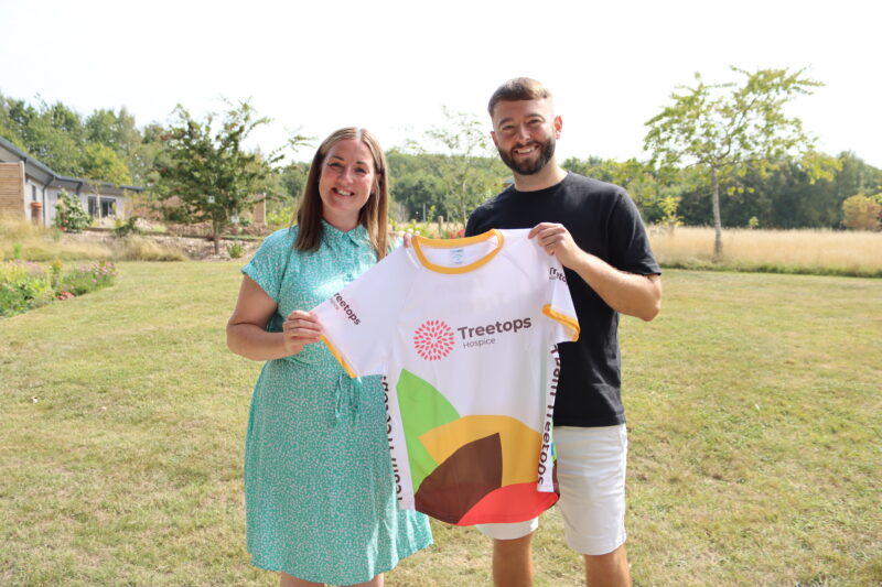 A man and woman smiling holding a T-shirt with a Treetops logo on it.