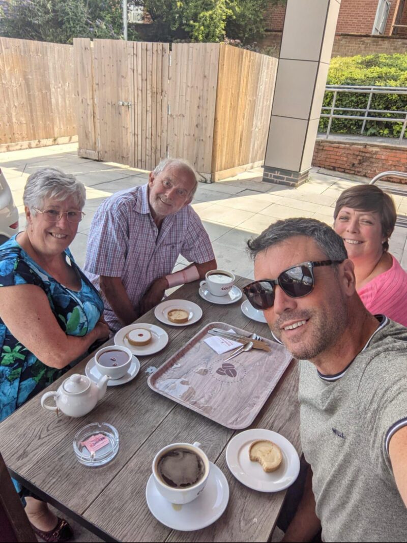 A family group sat around a table, drinking coffee outside on a sunny day.