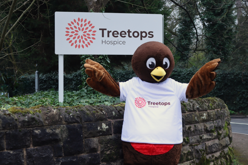 A happy robin mascot in front of a Treetops sign.
