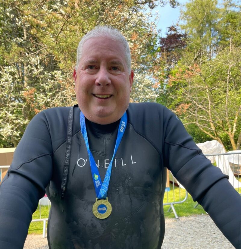 A man in a swimsuit smiling, wearing a medal around his neck.