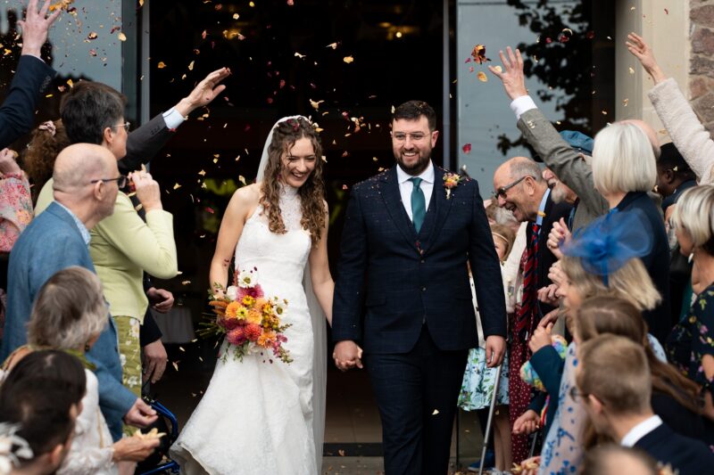 A bride and groom surrounded by family members throwing confetti on them.