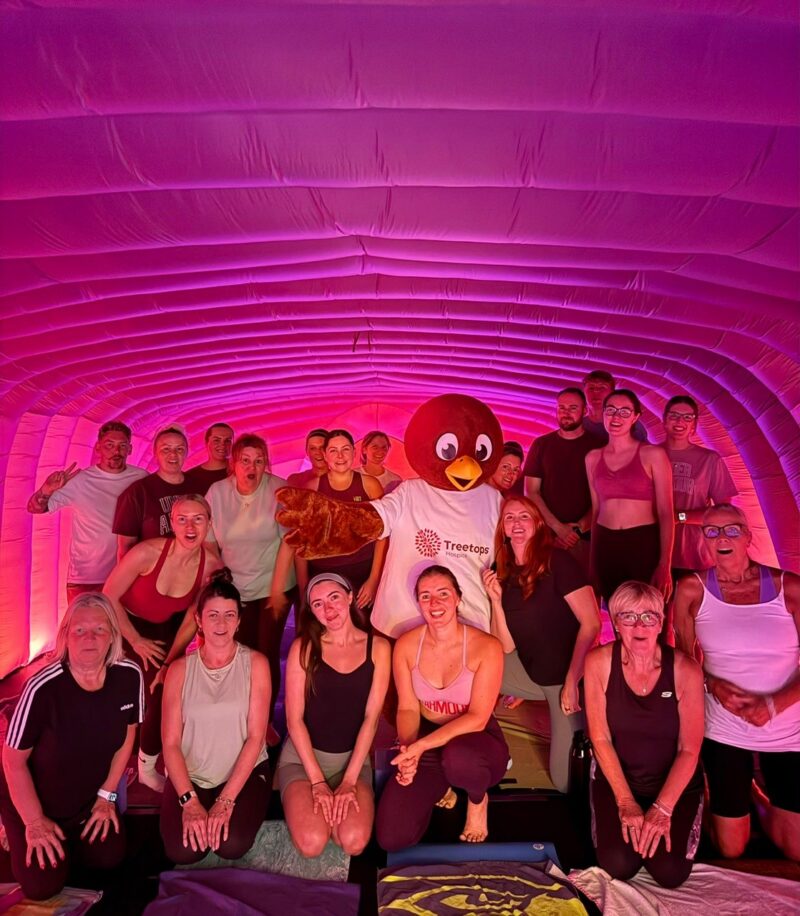A group of Hotpod Yoga attendees stood together in a purple pod with Remy, the Treetops mascot, in the middle.