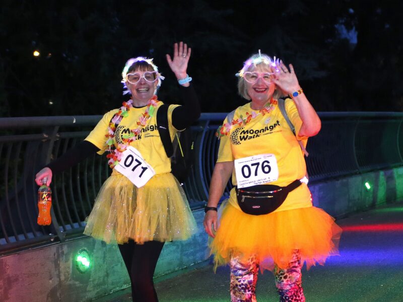 Two women wearing Moonlight Walk t-shirts, walking and smiling.