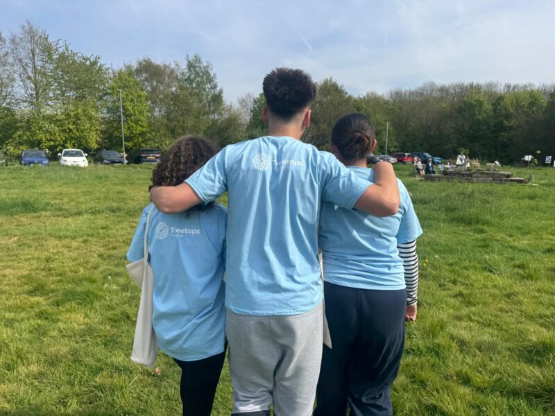 Three young people wearing Treetops Hospice t-shirts with their arms around each other.