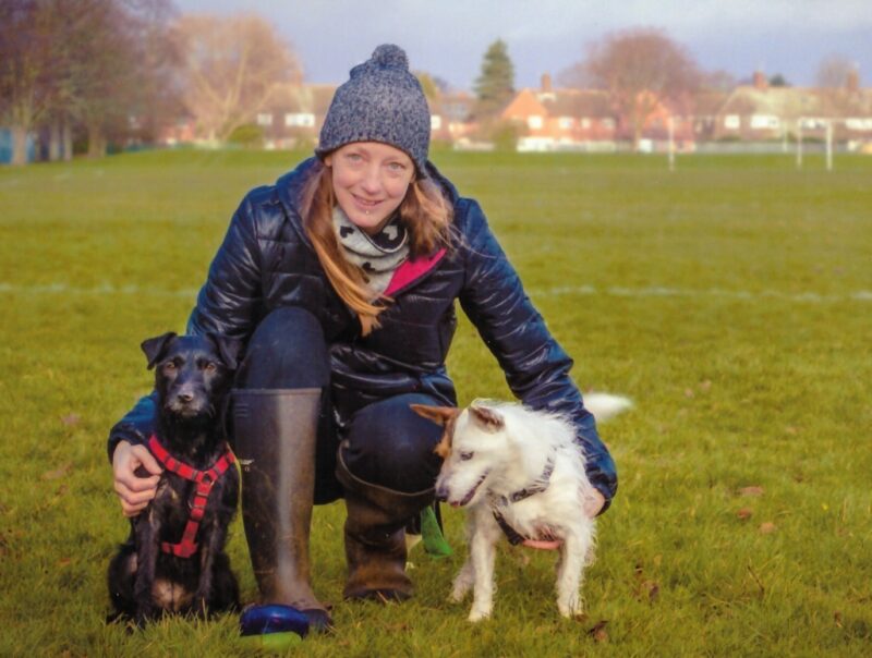 A woman crouching down with two small dogs.
